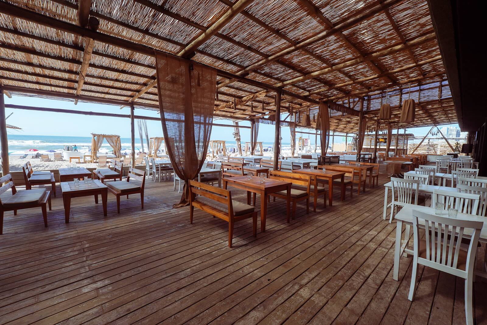 Salón de Roll & Rock con mesas de madera bajo techo de caña y vista al mar.
